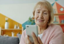 صورة توضيحية لسيدة مسنة تستخدم الهاتف في المنزل وليست إحدى ضحايا الاحتيال